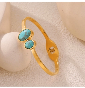 Detail of gold titanium steel open bangle featuring turquoise stones on a white sphere