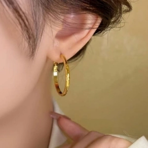 Détail d'une boucle d'oreille créole dorée à texture gaufrée portée à l'oreille