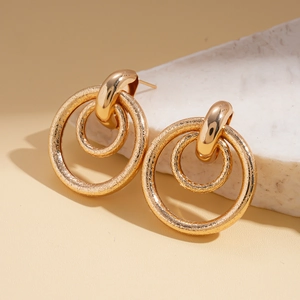 Detail of matte gold geometric hollow earrings with textured snakeskin surface finish
