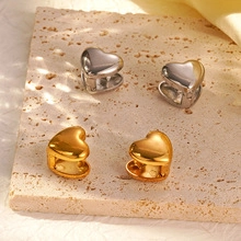 Macro detail of heart-shaped gold and silver earrings on a natural stone background