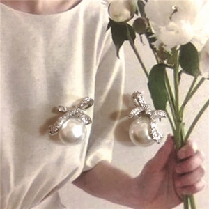 Macro detail of hand holding bow-knot pearl earrings with sparkling rhinestones decoration
