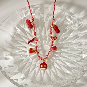 Détail artistique du collier en corde tressée rouge avec divers pendentifs en émail