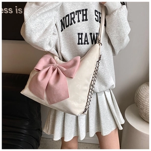 Detailed shot of the pink bow decoration and metallic chain strap on the cream shoulder bag
