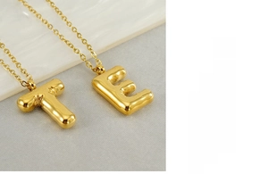 Détail macro des pendentifs lettres T et E dorés sur une chaîne O en acier inoxydable