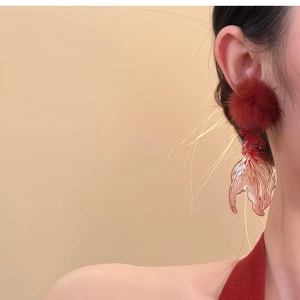 Macro detail of red fluffy pom-pom earring with hollow carp tail metal design
