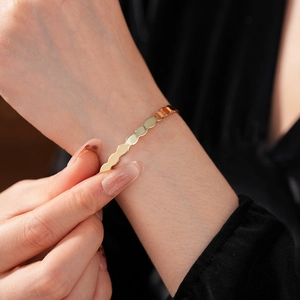 Detail showing wavy gold geometric open bangle with a polished mirror finish on wrist
