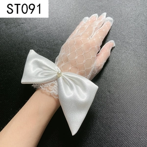 Close-up of white lace bridal gloves with large satin bow and pearl detail at wrist