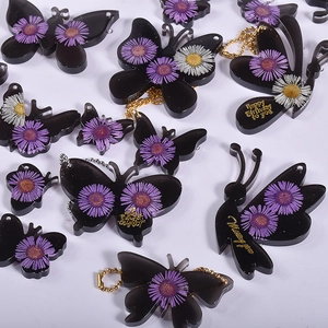 Detail of butterfly resin pendants with dried flowers and gold lettering on white base