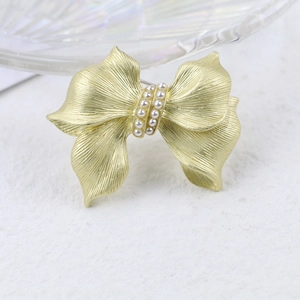 Elegant matte gold bow brooch with white pearl rows on textured white background