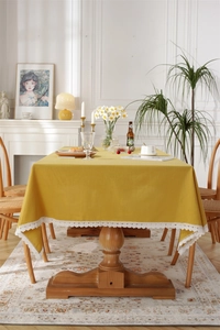 Detail of yellow cotton tablecloth with white lace edges on a wooden dining table