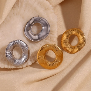 Detail view of gold and silver irregular textured hoop earrings on champagne silk