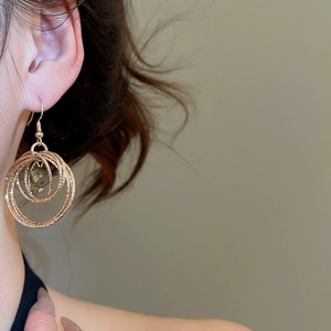 Detail view of gold layered hoop earrings with tiger eye stone on model's ear