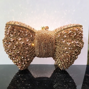Sparkling champagne gold bow evening clutch bag with dense rhinestones on black surface