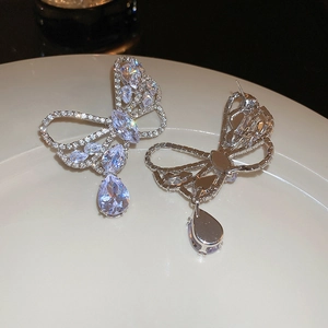 Macro view showing the silver bow earrings with zircon teardrop charms on a white plate