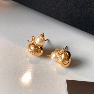 Vue macro de boucles d'oreilles gourde dorées avec perles blanches et cristaux brillants