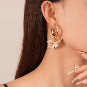 Gros plan d'un modèle portant d'élégantes boucles d'oreilles fleur en résine beige et or