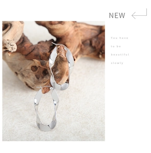 Close-up of polished silver twisted hoop earrings hanging on a natural wooden branch