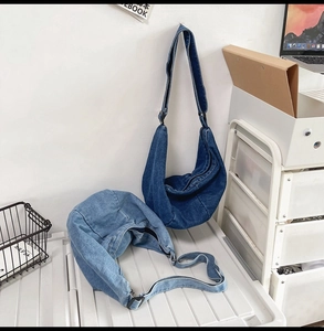Detail view of light and dark blue denim crescent bags with adjustable wide shoulder straps