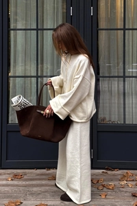 Detail of dark brown suede tote bag and cream knit outfit in a minimalist autumn setting