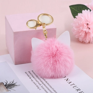 Detailed view of pink plush cat ear keychain with golden metal ring on pink background
