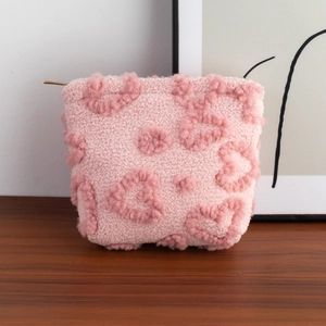 Detail of pink plush heart makeup bag with golden zipper on dark wooden surface