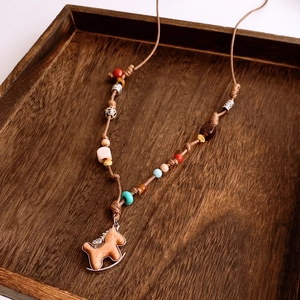 Detail of a handmade beaded necklace with a wooden rocking horse pendant on a tray