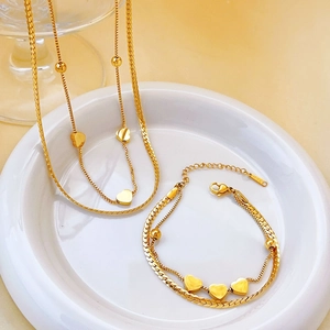 Double-layer gold heart pendant necklace and bracelet set in a white ceramic dish
