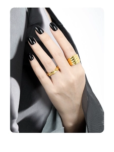 Detailed close-up of wide textured gold rings worn on hand with stylish black nails