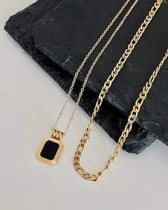 Detail of layered gold necklaces with black square pendant on textured stone background