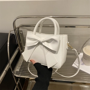 Elegant white bow handbag for women shown being held against a minimalist background
