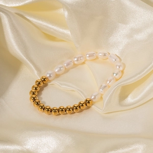 Détail d'un bracelet en perles d'eau douce et billes dorées sur du tissu en soie beige