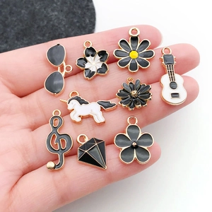 DIY black enamel alloy charms including flowers and musical notes held in hand for scale