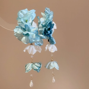 Détail de boucles d'oreilles fleurs en soie bleue avec perles fines et glands suspendus