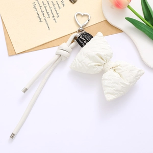 Close-up of a white quilted PU leather bow keychain with a silver heart-shaped clasp