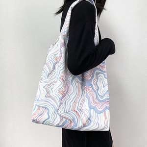 Detail of a large canvas tote bag with blue and red wave patterns shown on a shoulder