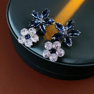 Close-up of flower stud earrings with blue and white zircon stones on jewelry case