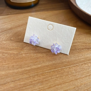 Macro detail of purple resin flower earrings on textured white card with wooden background