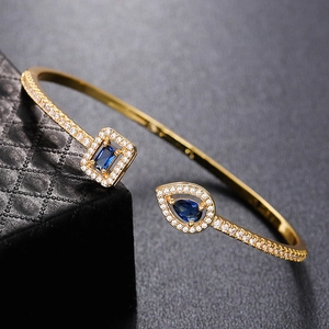 Detail of gold open bangle with blue stones on a black leather jewelry box