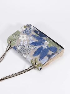 Macro detail of intricate floral embroidery and silver sequins on the woven shoulder bag