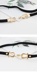 Detail of a thin elastic waist belt with a golden horseshoe buckle on a white background