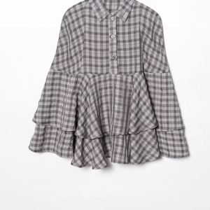 Vestido camisero de cuadros grises con mangas largas y dobladillo de volantes sobre fondo blanco