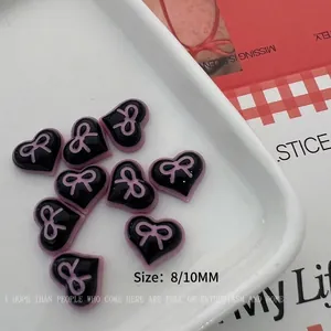 Macro shot of 8mm and 10mm black resin heart nail charms with pink bow accents