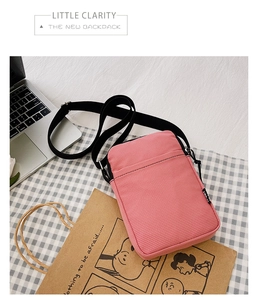 Detail view of pink corduroy crossbody phone bag with black adjustable strap on desk