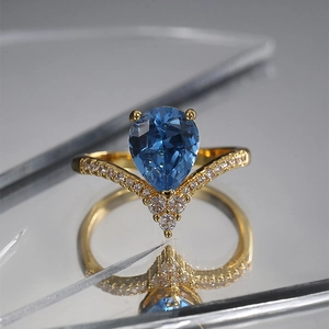 Retro gold V-shaped ring featuring a water drop blue zircon on a reflective surface