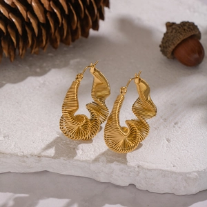 Irregular twisted gold hoop earrings on stone surface with pine cones for autumn style