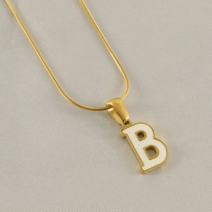 Close-up of golden snake chain necklace with white enamel letter B pendant on grey silk