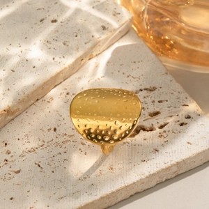 Golden stainless steel heart ring with textured finish on a minimalist stone surface