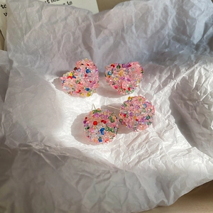 Macro view of pink heart and sphere resin earrings with colorful glitter filling