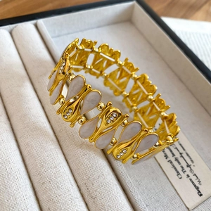 Detail of gold elastic bracelet with enamel leaf charms and rhinestones on jewelry tray