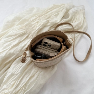 Sac seau chic en paille beige avec détails en dentelle et bandoulière sur fond plissé